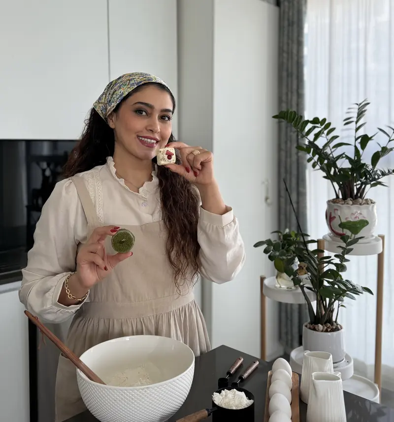 Nasi in her kitchen, smiling and holding two small cakes